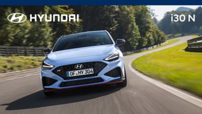 The new Hyundai i30 N from the front in Performance Blue colour driving down a race track.	